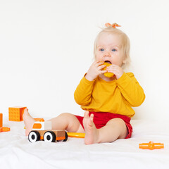 A little Caucasian girl is playing with toys on a white background. 1 year old, the child is wearing an orange T-shirt and playing with orange toys. High quality photo
