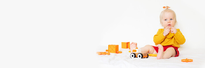 A little Caucasian girl is playing with toys on a white background. 1 year old, the child is wearing an orange T-shirt and playing with orange toys. High quality photo
