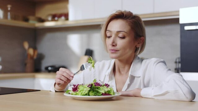 Tired woman sitting at table looking sad and bored with diet don't want to eat salad. At the kitchen. Food. Portrait. Slow motion