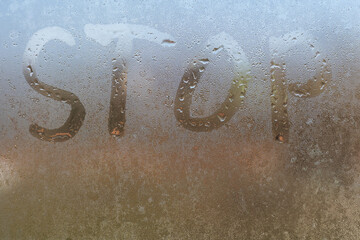 the word stop written on night wet window glass close-up with blurred background