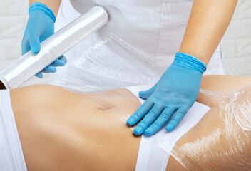 The masseur does a full body wrap cosmetic procedure in a beauty salon. Spa treatment in a beauty salon - obrazy, fototapety, plakaty