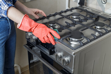modern gas oven. a girl in red rubber gloves washes a gas stove with a sponge. girl in jeans and a blue plaid shirt. Cleaning in the kitchen.