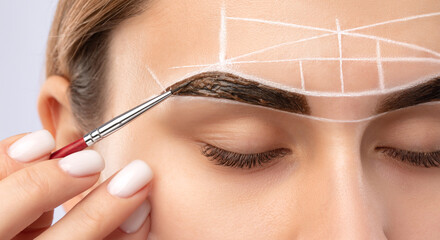 Make-up artist makes markings with white pencil for eyebrow and paints eyebrows. Professional...