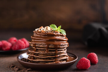 Stack of chocolate pancakes with sauce and raspberries