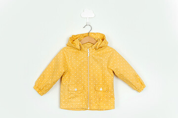 Yellow raincoat hanging on a hanger. Stylish childrens outerwear on white background. Autumn kids...