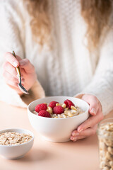 Bowl of oatmeal porridge with raspberries and cashew in female hands. Concept of clean eating, dieting, veganism