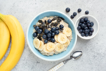 Oatmeal bowl with banana, blueberry and pumpkin seeds on grey cement background. Table top view