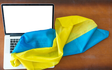 Laptop with blank screen on table and Ukrainian national flag on background, space for text.