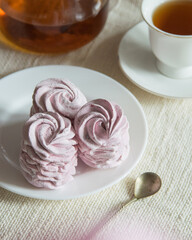 Homemade russian marshmallow - zephyr on white plate with a cup of tea on light linen tablecloth, selective focus