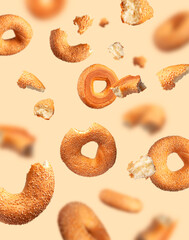 Creative food, baking layout. Fresh round wheat bagel with sesame seeds flying on beige background....