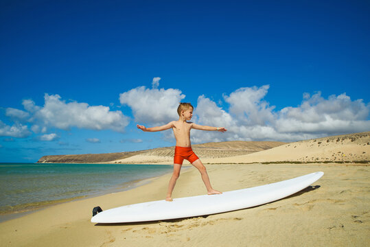Boy on the beach is standing on a surfboard. learning to surf.