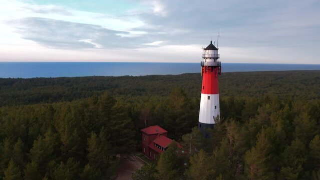 Aerial view of the lighthouse. Sea in the background. Slow drone flight low over the green lush forest.