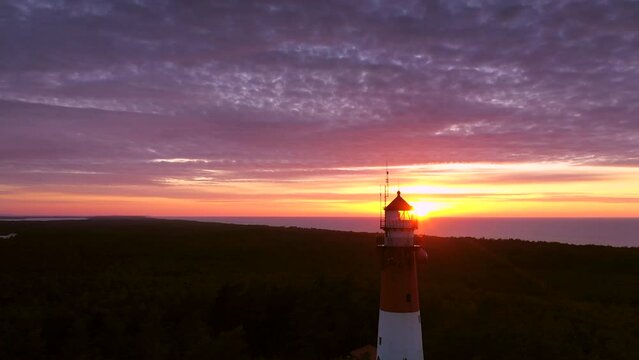 Beautiful sunset over green forest. View of the lighthouse. Orange sun, pastel pink clouds, red sky. Zoom out.