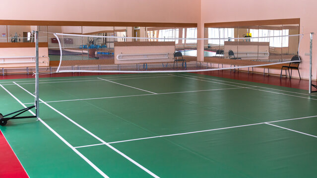 Sports hall with a white woven net. Badminton court. Sports hall for sports. A green sports ground with white markings and mirrors.