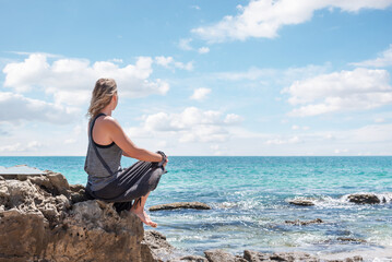 Caucasian blonde woman sitting on a rock contemplating the sea. Meditation and relaxation in the open air