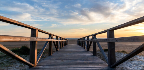 Obraz premium Panoramic view of a wooden walkway leading to the beach at sunset with a beautiful cloudy sky