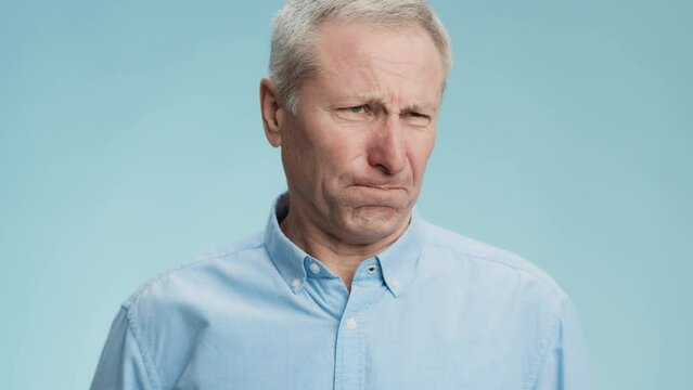 Disgust feeling. Emotional grey haired senior man feeling unpleasant smell, frowning face and gagging, blue background