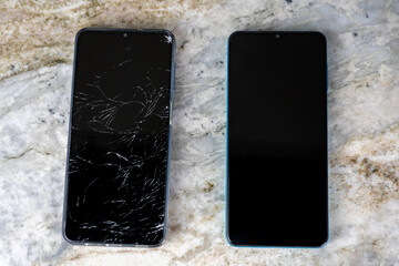 Smartphone with cracked screen and mobile phone with intact touchscreen lying on marble surface