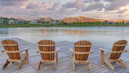 Panorama Puffy clouds at sunset Four wooden lounge chairs facing the reflective Oquirrh Lake at