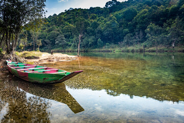 isolated wood boat with water refection at calm river surrounded by dense green forests at morning
