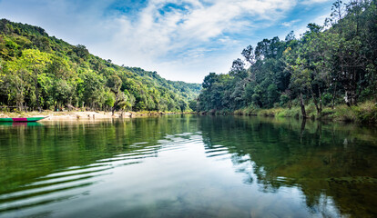 calm river surrounded by dense green forests and blue sky with water refection at morning