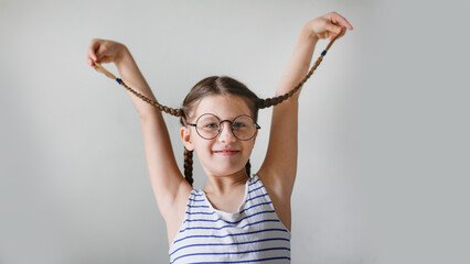 Fototapeta na wymiar Funny crazy girl child schoolgirl with pigtails in round glasses with hands, copy space and light beige background