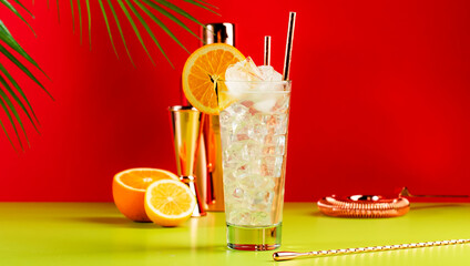 Tom Collins popular alcoholic cocktail with dry gin, syrup, lemon juice, soda, orange and ice. Bright red green summer banner background, negative space