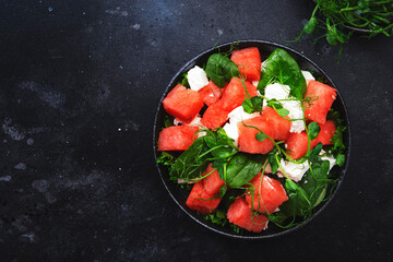 Delicious summer watermelon salad bowl with feta cheese, spinach and pea sprouts on gray table background, top view, negative space