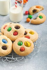 Homemade cookies with colorful chocolate candies and milk. Stack of shortbread cookies with multi colored candy on plate with bottle of milk on light gray background. Baby food concept. Copy space.