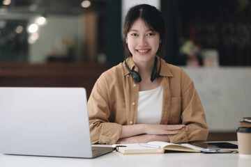 Happy young Asian student woman wearing headphones looking at webcam, looking at camera, during virtual meeting or video call talk.