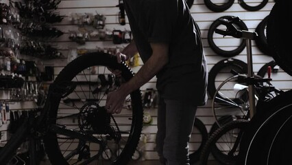 Young bicycle repair service engineer makes diagnosis and puts wheel on frame. Repair service for sports and mountain bikes. Sports shop and service center for repair of sports equipment