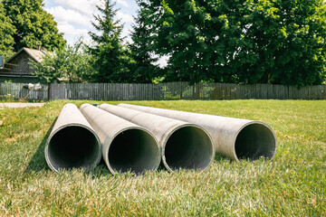 Chrysotile cement pipes lie on the green grass of construction site. Four round tubes. Copy space. Building element. Column concept. Drainage material. Large sewerage culvert. Industrial engineering