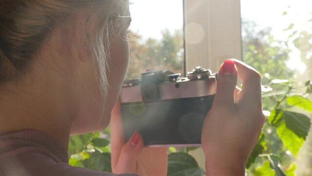 Young woman with blond curly hair photographs nature through the window