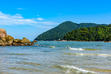 Naklejka premium The sea with calm and transparent waters between the rocks, mountains and tropical forests of Bertioga on the coast of Sao Paulo, Brazil