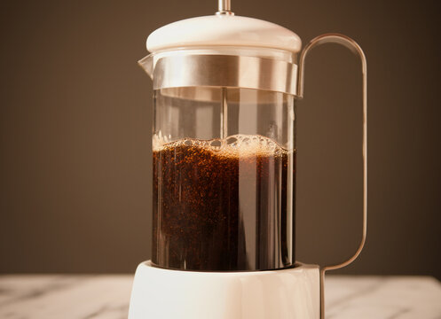 Fresh coffee in a coffee press alongside biscuits and a cup of coffee.