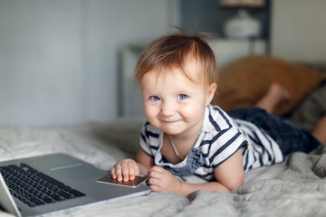 Fototapeta premium Toddler baby with laptop and bank card, online shopping and kids, toddler with laptop on bed in bedroom