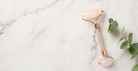 Skincare concept. Top view photo of rose quartz roller and eucalyptus on white marble background...