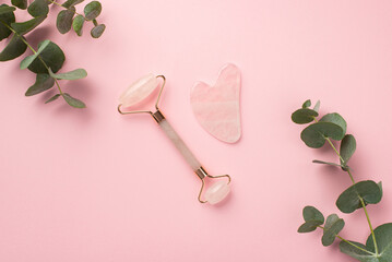Top view photo of eucalyptus leaves rose quartz roller and gua sha massager on isolated pastel pink...