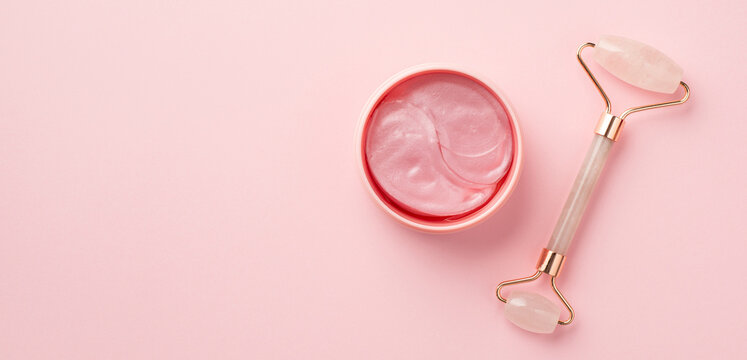 Top view photo of rose quartz roller and pink eye patches on isolated pastel pink background with copyspace