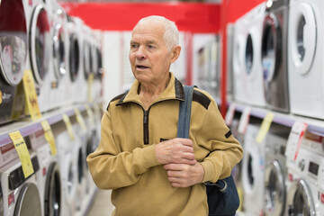 elderly man choosing washing machine in showroom of electrical appliance store