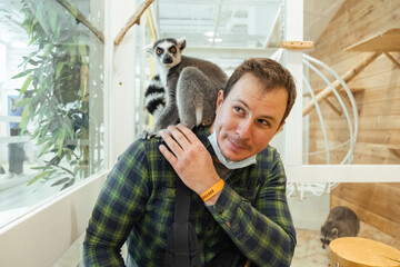 Portrait of young caucasian man smiling while holding lemur on his shoulder in the zoo © alexanderon