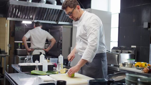 Male chef in uniform cutting fresh leeks while cooking food order in restaurant kitchen