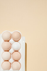 fresh beige chicken eggs in an egg box on a beige background