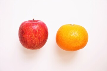 白背景に並べられた赤い一つのリンゴとオレンジ色のミカン