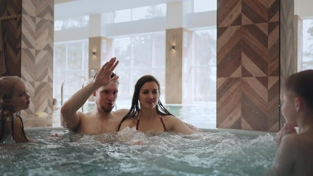 family with kids is resting in thermal bath of modern wellness center, children and parents are relaxing in jacuzzi