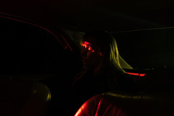a girl is driving a car at night, she is illuminated by red and yellow night lights