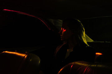a girl sits in a car with a leather interior at night, it is dark, night lights, red and yellow lights on the road.