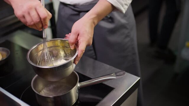 Cropped shot of professional male chef melting butter in steel bowl with whisk on boiling water bath