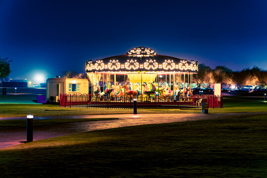 Doha, Qatar - Apr. 2020: Carousel with horses, also known as a merry-go-round, illuminated with bright warm light. No people. View at night.