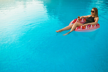 Woman with red glass of wine relaxing in swimming pool.